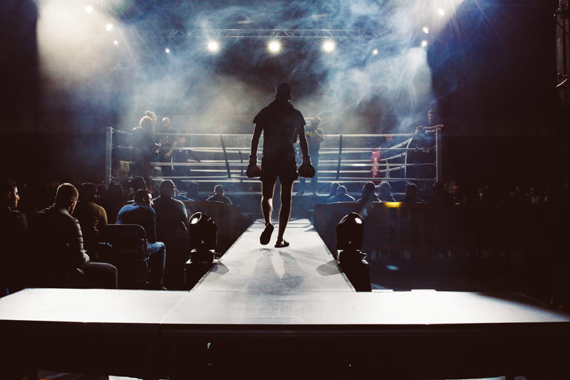 A Muay Thai fighter walks out to the ring under lights.