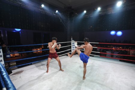 Two Muay Thai fighters compete in the ring in front of a crowd.